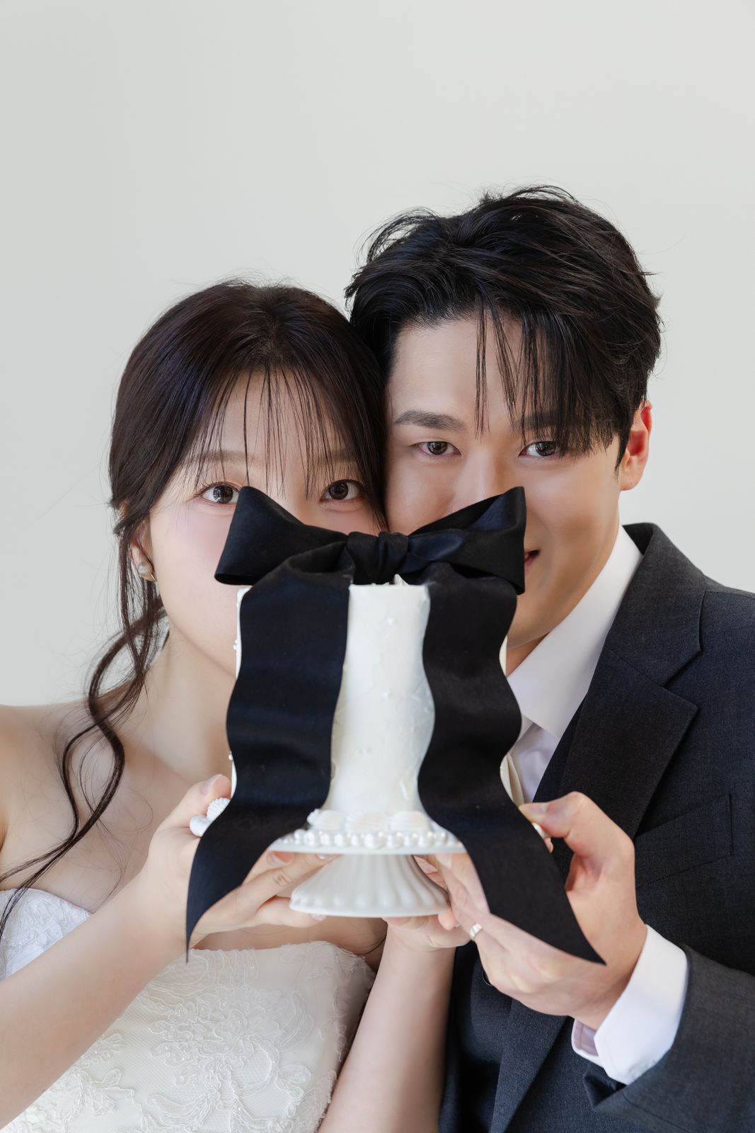 검은 리본을 두른 케이크를 함께 들고 얼굴을 반쯤 가린 신랑 신부